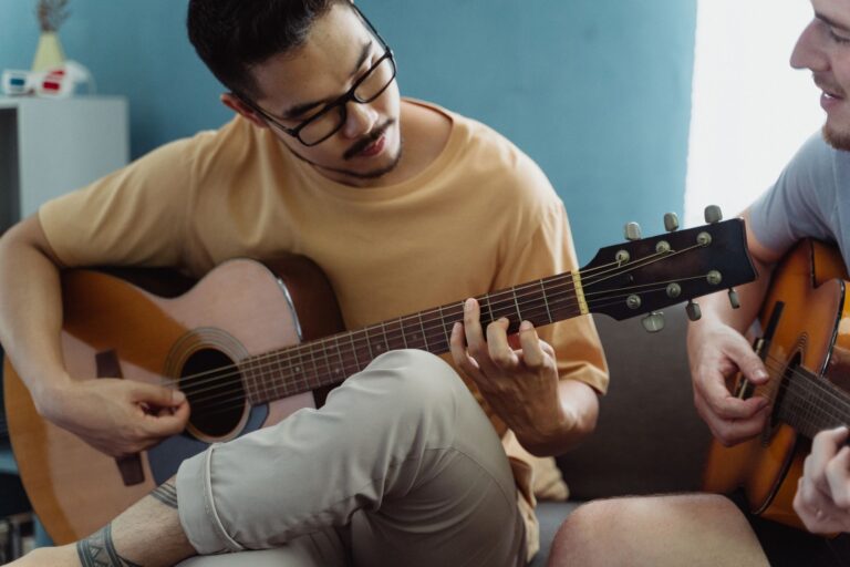 Dois homens tocando violao lado a lado em ambiente iluminado, ilustrando a musica como forma de conexao e bem-estar